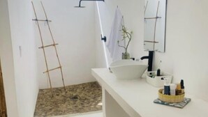Een badkamer met een wit wastafel, spiegel en handdoekhouder. Er is een klein raam en een douchegedeelte met een handdoek.
