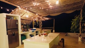 Een keuken met een koelkast, een aanrecht met een fruitschaal en een rustiek plafond met lichtjes.