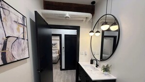 Un baño moderno con un lavamanos blanco, armarios negros, un espejo redondo y una lámpara en el techo.