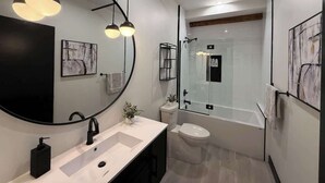 Un baño moderno con un espejo grande, dos lámparas colgantes, una bañera y un inodoro.