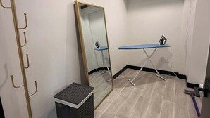 Una habitación con un espejo de pie, una mesita pequeña, un cesto de basura y una tubería en el techo.