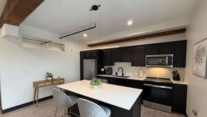Una cocina moderna con armarios oscuros, una isla blanca, electrodomésticos de acero inoxidable y una viga de techo de madera.