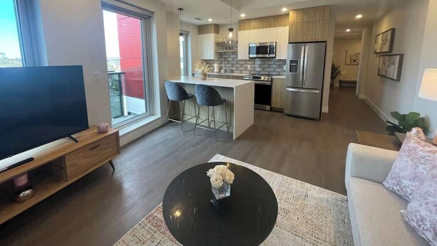 A modern living room with a flat-screen TV, a coffee table with flowers, and a sofa. - Downtown, Spotless 2 Bed, 2 Bath with 6 appliances (Halifax)