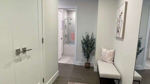 A hallway with a white door, a bench, a potted plant, and a mirror on the wall. - Downtown, Spotless 2 Bed, 2 Bath with 6 appliances (Halifax)