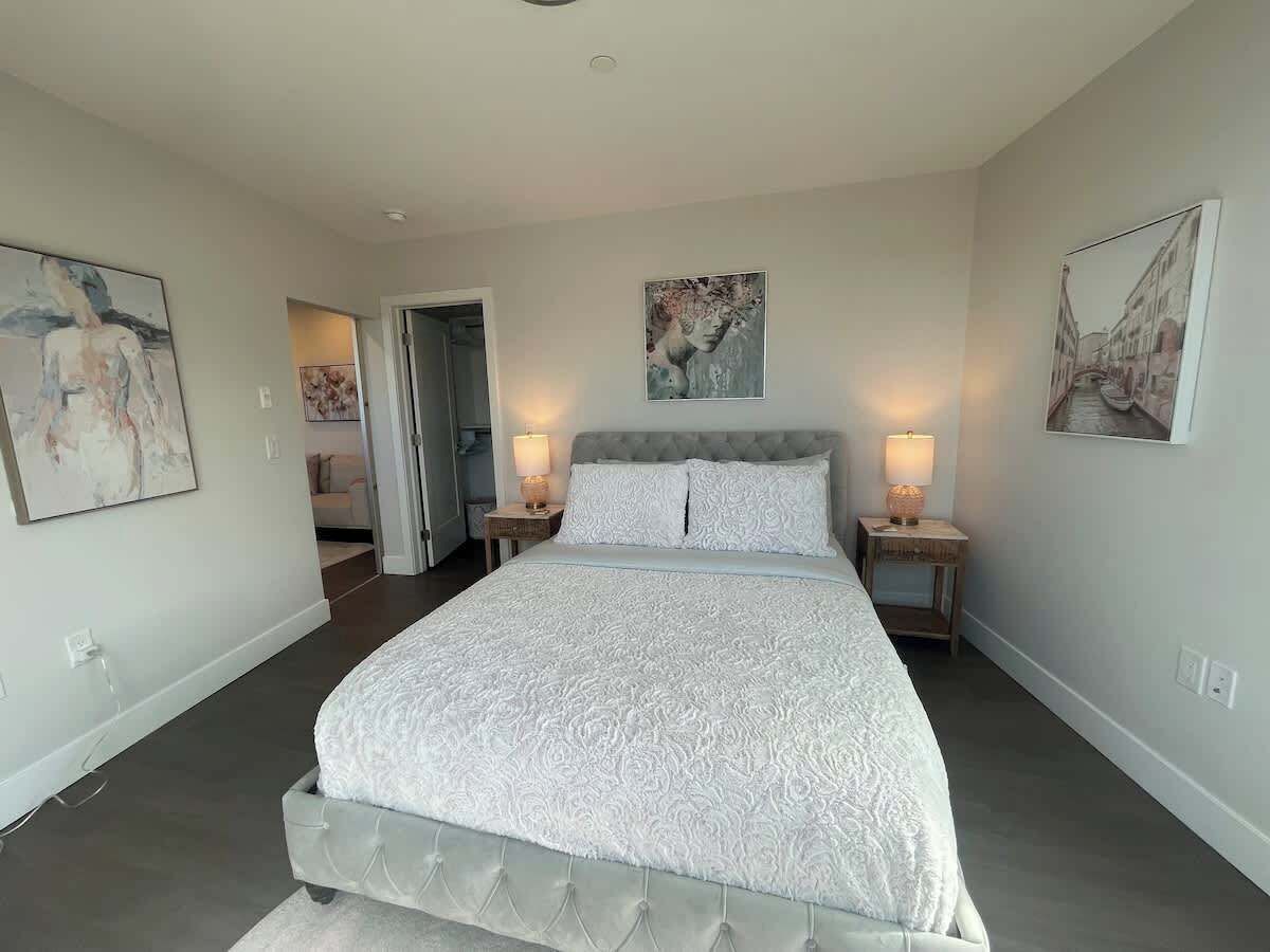 A bedroom with a large bed, two bedside tables with lamps, and three framed artworks on the walls.