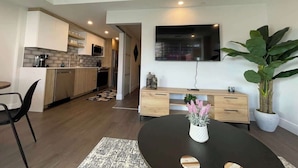 A modern kitchen with a dining area, a flat-screen TV mounted on the wall, and a large potted plant. - Large 1 BR downtown with lots of sunlight (Halifax)