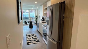 A modern kitchen with wooden cabinets, a stainless steel refrigerator, and a dining area with a table and chairs. - Large 1 BR downtown with lots of sunlight (Halifax)