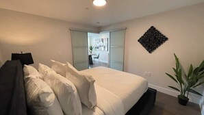 A modern bedroom with a large bed, a desk, and a potted plant. - Large 1 BR downtown with lots of sunlight (Halifax)