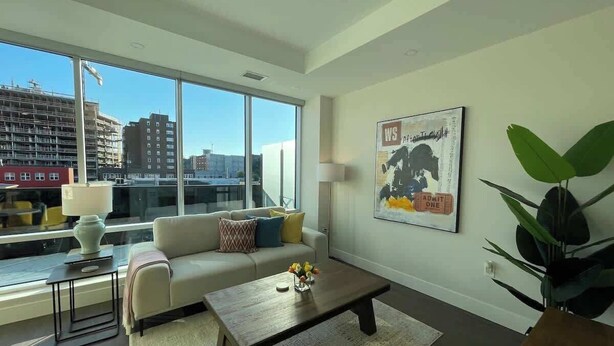 A modern living room with a sofa, coffee table, and a large window offering a city view.