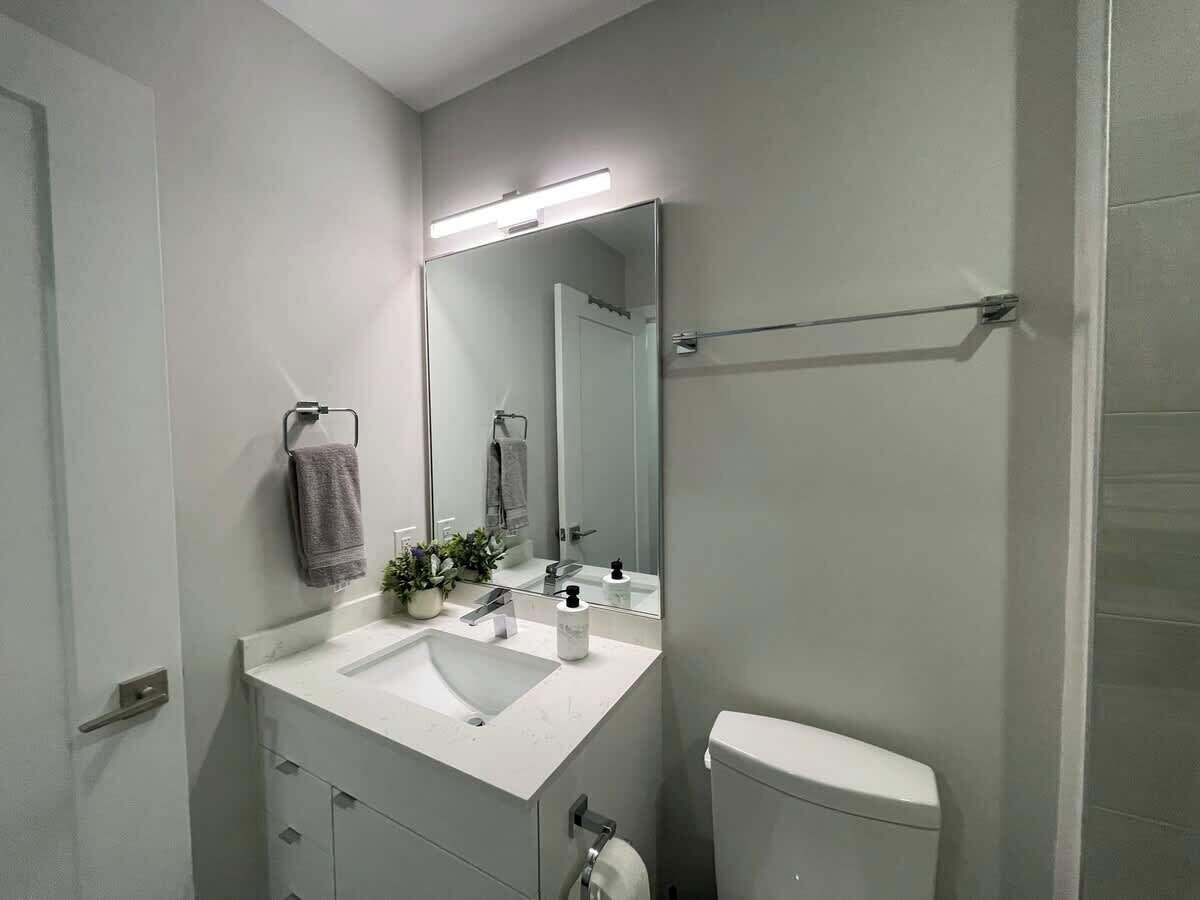 Een moderne badkamer met een wit wastafelmeubel, een spiegel, een handdoekhouder en een toilet.