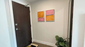 A hallway with a dark door, a potted plant, and two abstract paintings on the wall.