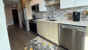 A modern kitchen with a stainless steel refrigerator, microwave, stove, and dishwasher. There is a wooden cabinet and a white countertop.