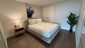 A bedroom with a bed, bedside table, lamp, and a large potted plant. - Downtown, Waterfront 1 Bedroom with AC and Gym (Halifax)