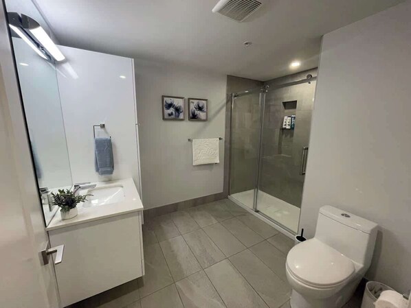 A modern bathroom with a glass shower enclosure, a white toilet, and a sink with a mirror.