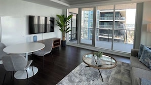 A modern living room with a round dining table, grey chairs, a sofa, a coffee table, and a large window with a city view.
