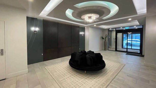 A spacious lobby with a modern ceiling design, a central seating area, and a view of the outside through a glass door.