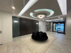 A spacious lobby with a modern ceiling design, a central seating area, and a view of the outside through a glass door.