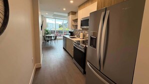 A modern kitchen with stainless steel appliances, a dining area with a table and chairs, and a view of the outdoors.