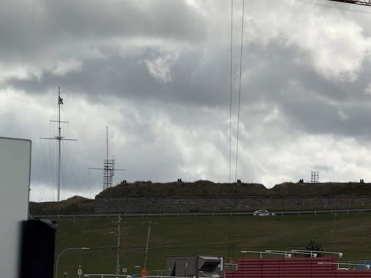 A stadium with a grassy field, bleachers, and a car parked in the foreground.