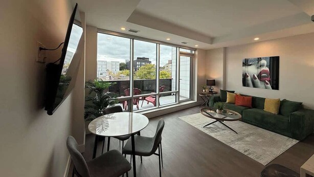 A modern living room with a large window, a green sofa, a round coffee table, and a dining area with chairs.