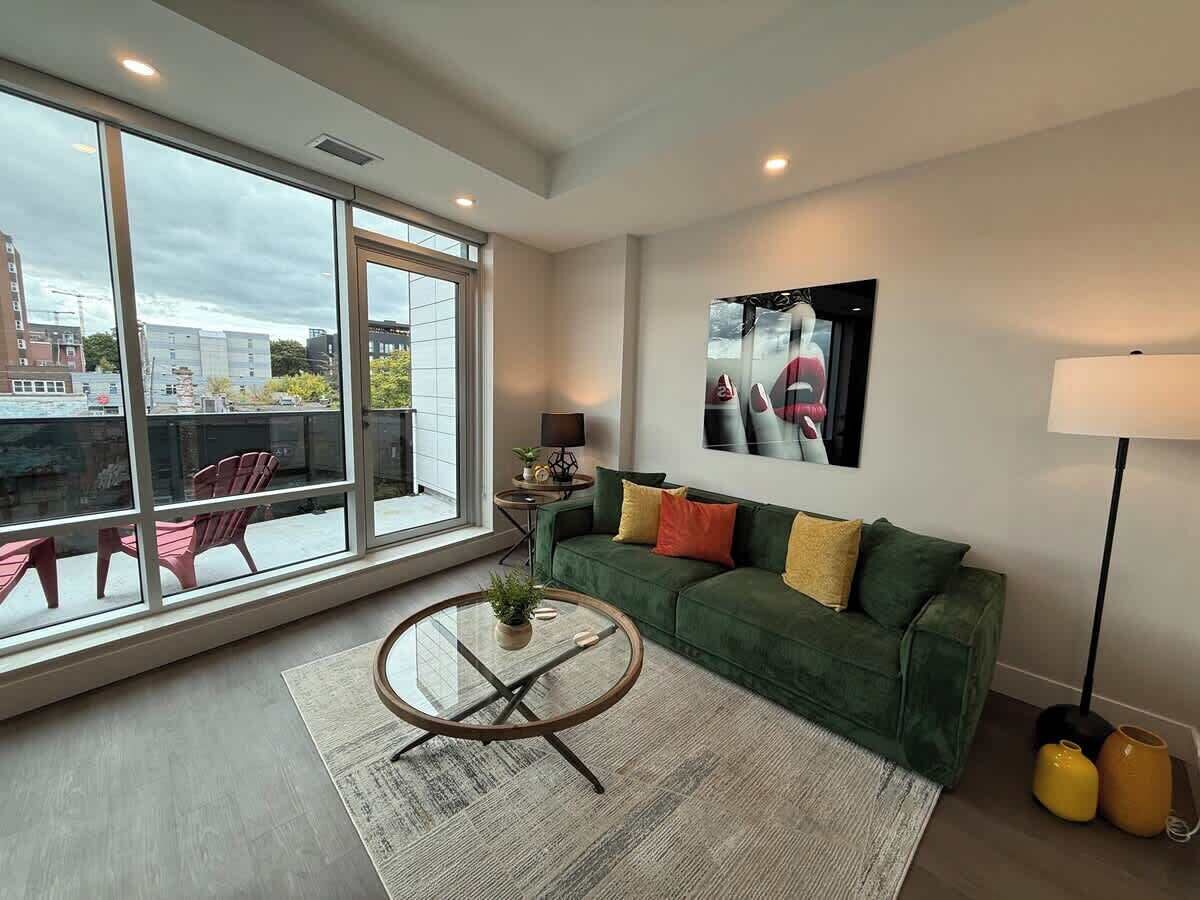 A modern living room with a green sofa, a round coffee table, and a large window offering a view of the city.
