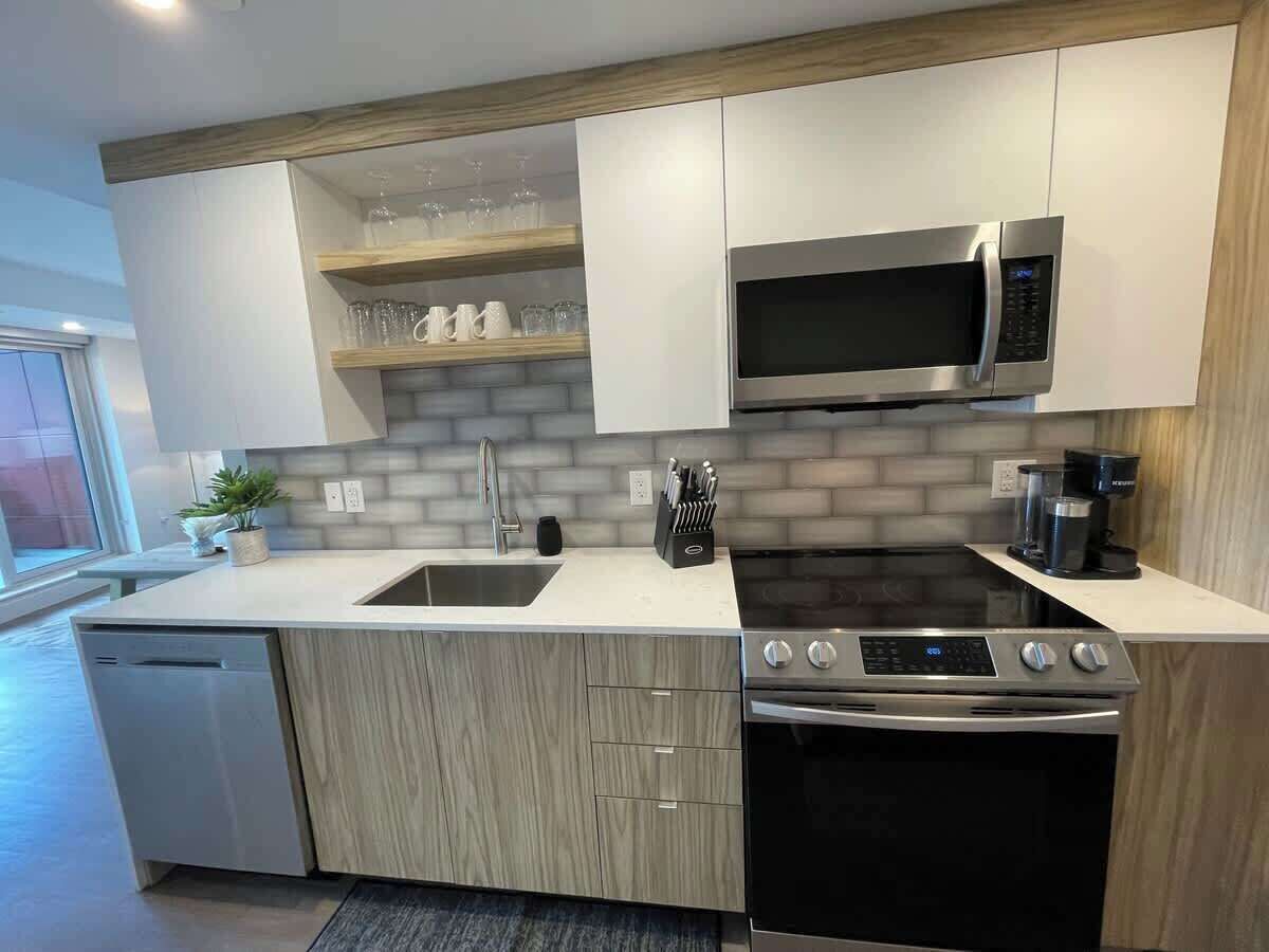 A modern kitchen with a dishwasher, stove, microwave, and a sink.