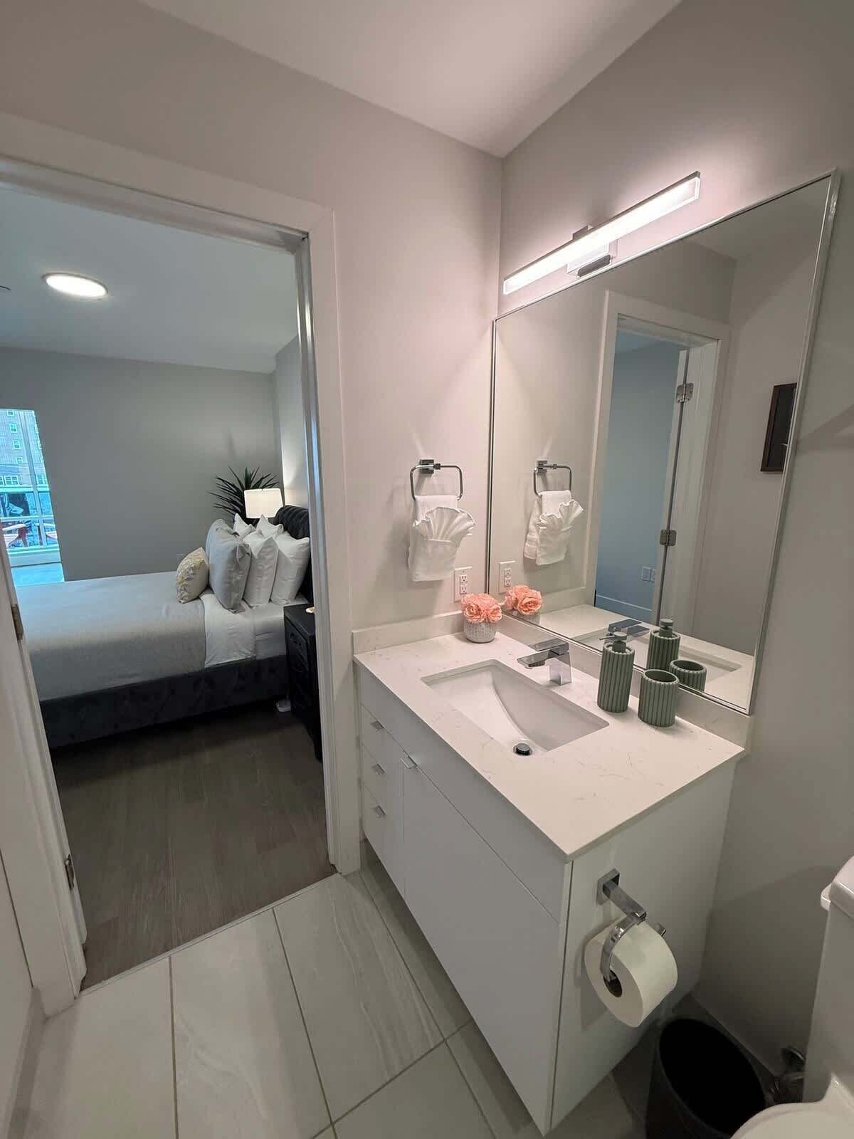 A modern bathroom with a large mirror, white sink, and a toilet.