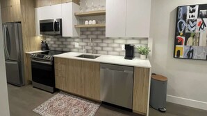 A modern kitchen with stainless steel appliances, wooden cabinets, a white countertop, and a small sink.