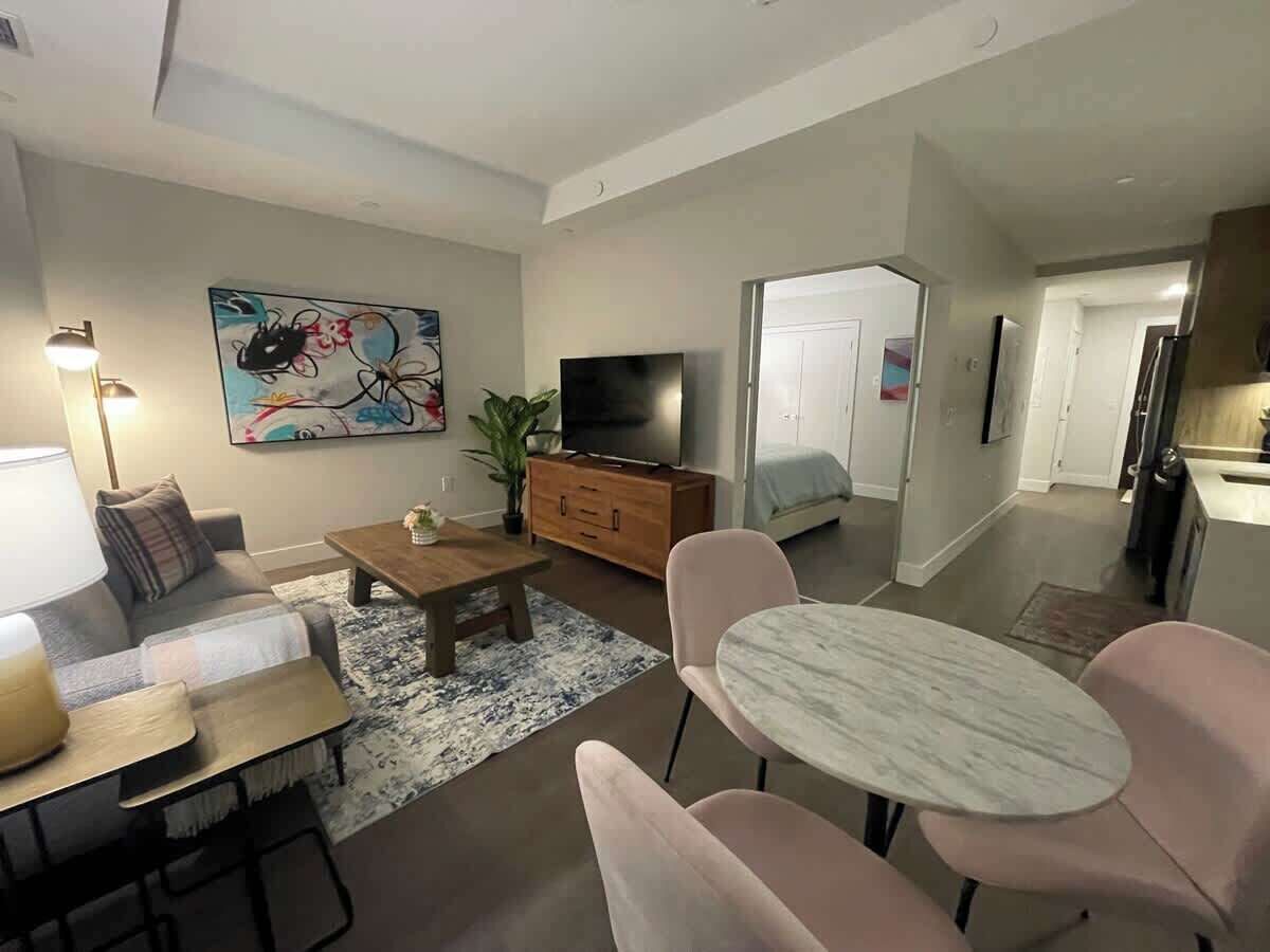 A modern living room with a sofa, coffee table, TV, and dining area.