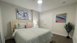 A bedroom with a bed, a nightstand, a dresser, a closet, and a painting on the wall.
