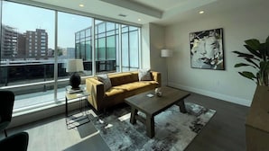 Un salon moderne avec un canapé, une table basse et un lampadaire. De grandes fenêtres offrent une vue sur le paysage urbain.