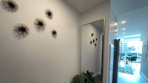 Un couloir avec un grand miroir qui reflète les décorations du plafond, une plante en pot et une vue sur une salle à manger.