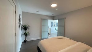 Une chambre moderne avec un grand lit, une plante en pot et une porte coulissante donnant sur un balcon.