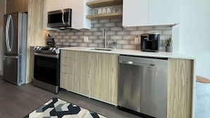 Une cuisine moderne avec des meubles de rangement en panneaux de bois, des appareils électroménagers en acier inoxydable et un four à micro-ondes encastré.