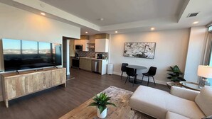 A modern living room with a flat-screen TV, a sofa, a coffee table with a plant, and a dining area with chairs. - Waterfront penthouse 1 Bedroom with 6 appliances (Halifax)