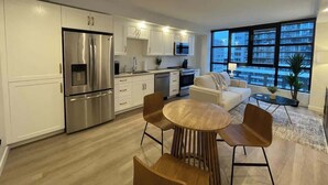A modern kitchen with white cabinets, stainless steel appliances, and a dining area with a round wooden table and brown chairs.