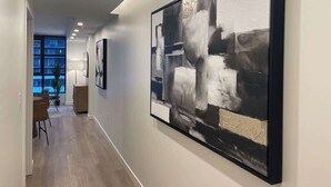 A hallway with abstract paintings on the walls, a dining area with chairs and a table, and a view of the outside through a window.