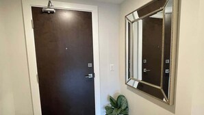 Una puerta de madera oscura con un picaporte plateado, un espejo adosado a la pared con un marco decorativo y una planta en maceta sobre una superficie de madera.