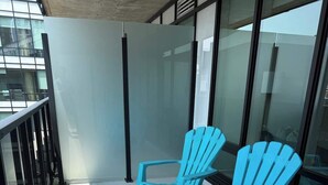 Deux chaises Adirondack bleues sur un balcon doté d’une rambarde en verre et d’un sol en béton.