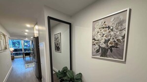 Un couloir avec un miroir, une plante en pot et une œuvre d’art encadrée accrochée au mur.