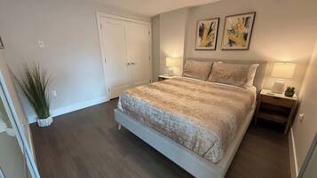 Une chambre à coucher avec un grand lit, deux tables de chevet avec des lampes, une porte et une plante en pot.
