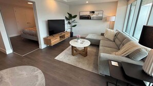 A modern living room with a sofa, a coffee table, a TV, and a plant. - Bright, spotless and modern 1 BR with gym (Halifax)