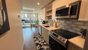 A modern kitchen with a built-in microwave, stove, and sink. There is a dining area with a table and chairs visible in the background. - Bright, spotless and modern 1 BR with gym (Halifax)