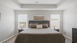 Une chambre à coucher comprenant un lit, deux tables de chevet, une commode, une tête de lit et une fenêtre avec des stores.