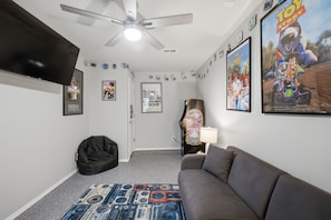 A room with a ceiling fan, a flat-screen TV, a bean bag chair, a couch, and various movie posters on the walls. - Family-friendly 3BR home with a fun game room, fenced yard, patio, and extra sleeping space—perfect for groups and longer stays. (Broken Arrow)