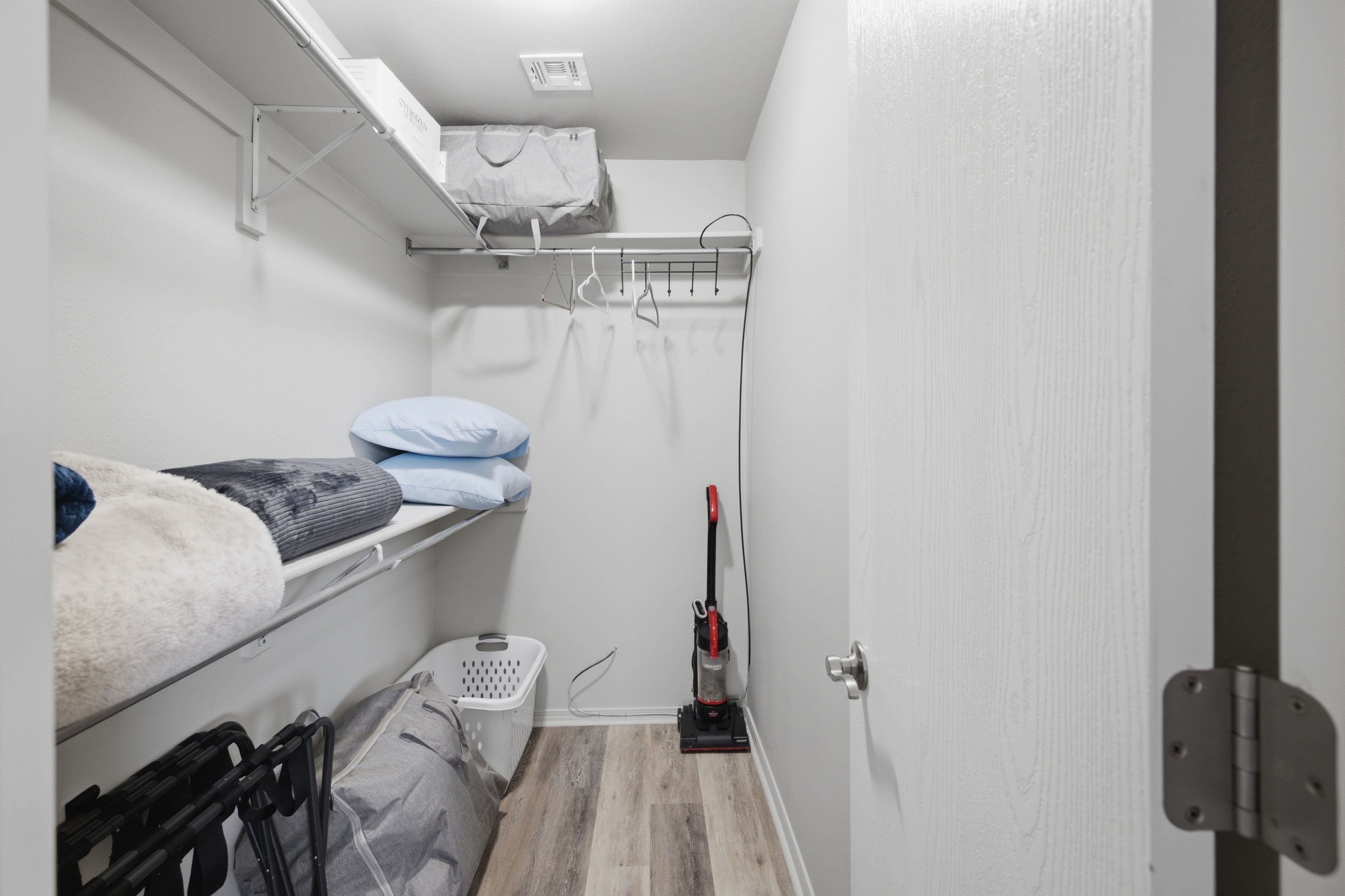 Une petite pièce avec des lits superposés, un aspirateur et un panier à linge.