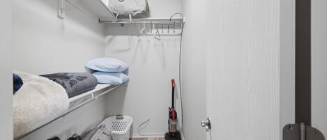Une petite pièce avec des lits superposés, un aspirateur et un panier à linge.