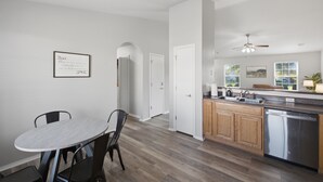 Une cuisine moderne avec des meubles en bois, un lave-vaisselle en acier inoxydable et un coin repas comprenant une table ronde et des chaises.