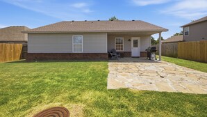 Une maison de plain-pied avec un patio en pierre, des fondations en briques et une clôture en bois.