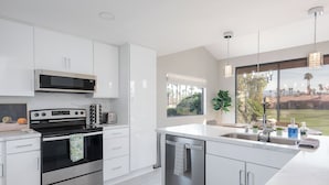 A modern kitchen with white cabinetry, stainless steel appliances, and a large window offering a view of the outdoors.